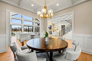 A dining area with a round table, six chairs, a chandelier, and a view of the outdoors. - Serene Lakefront Lake Anna, Beach, Dock, Pool (Louisa County)
