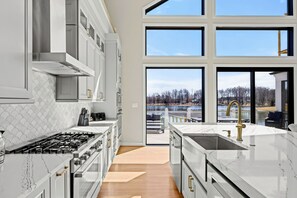 A modern kitchen with a large island, stainless steel appliances, and a view of a lake through large windows.