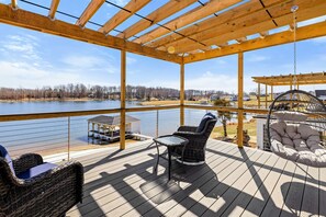 A covered deck with a view of a lake, outdoor furniture, and a swing chair.