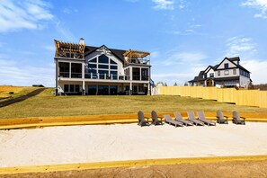 Une grande maison à deux étages avec un balcon, une cour clôturée et des chaises de plage.