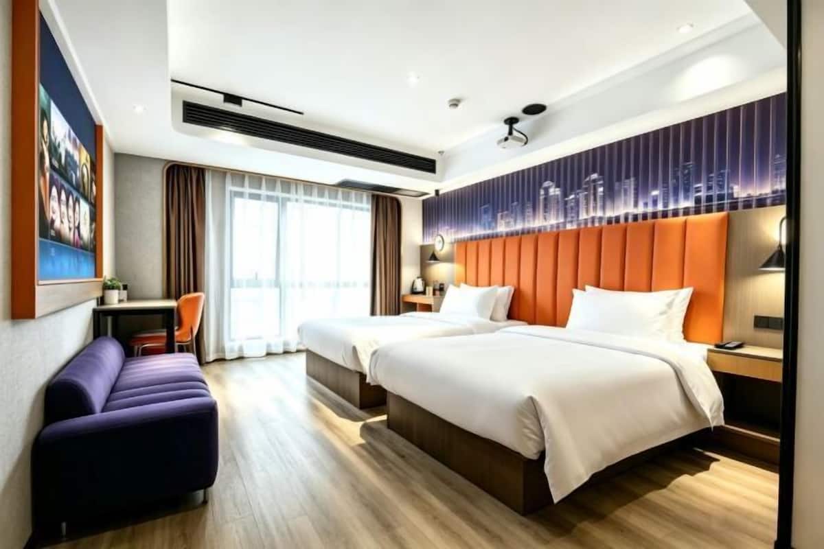 A hotel room with two beds, a sofa, a desk, and a cityscape view.
