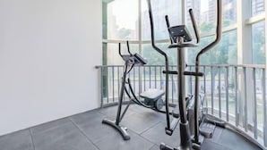 Een sportschool met twee elliptische trainers en een loopband, grote ramen en een balkon met een hekwerk.