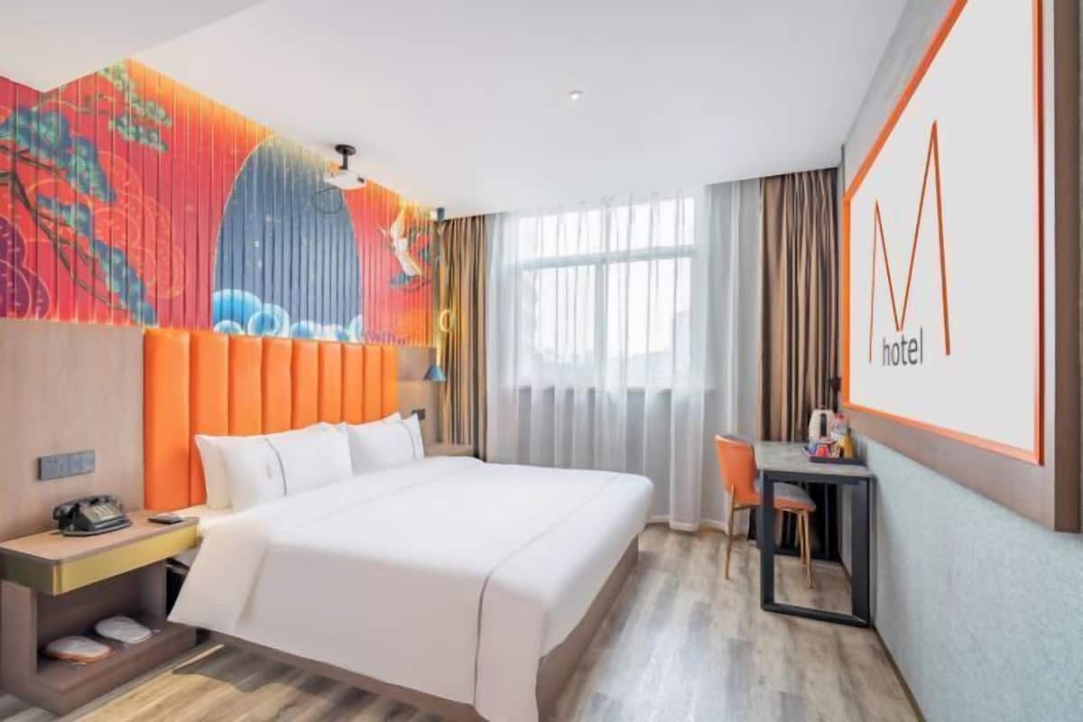 A hotel room with a bed, a desk, a chair, a phone, and a wall with a colorful mural.