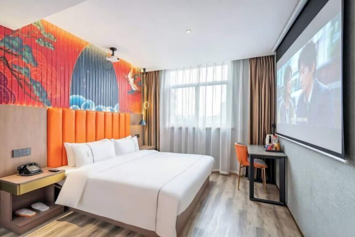 A hotel room with a bed, a desk, a chair, a television, and a window.
