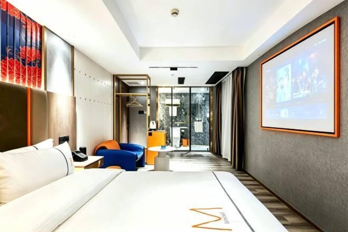 A modern hotel room with a large bed, a seating area with a blue sofa, a small table, and a large screen displaying a slideshow.