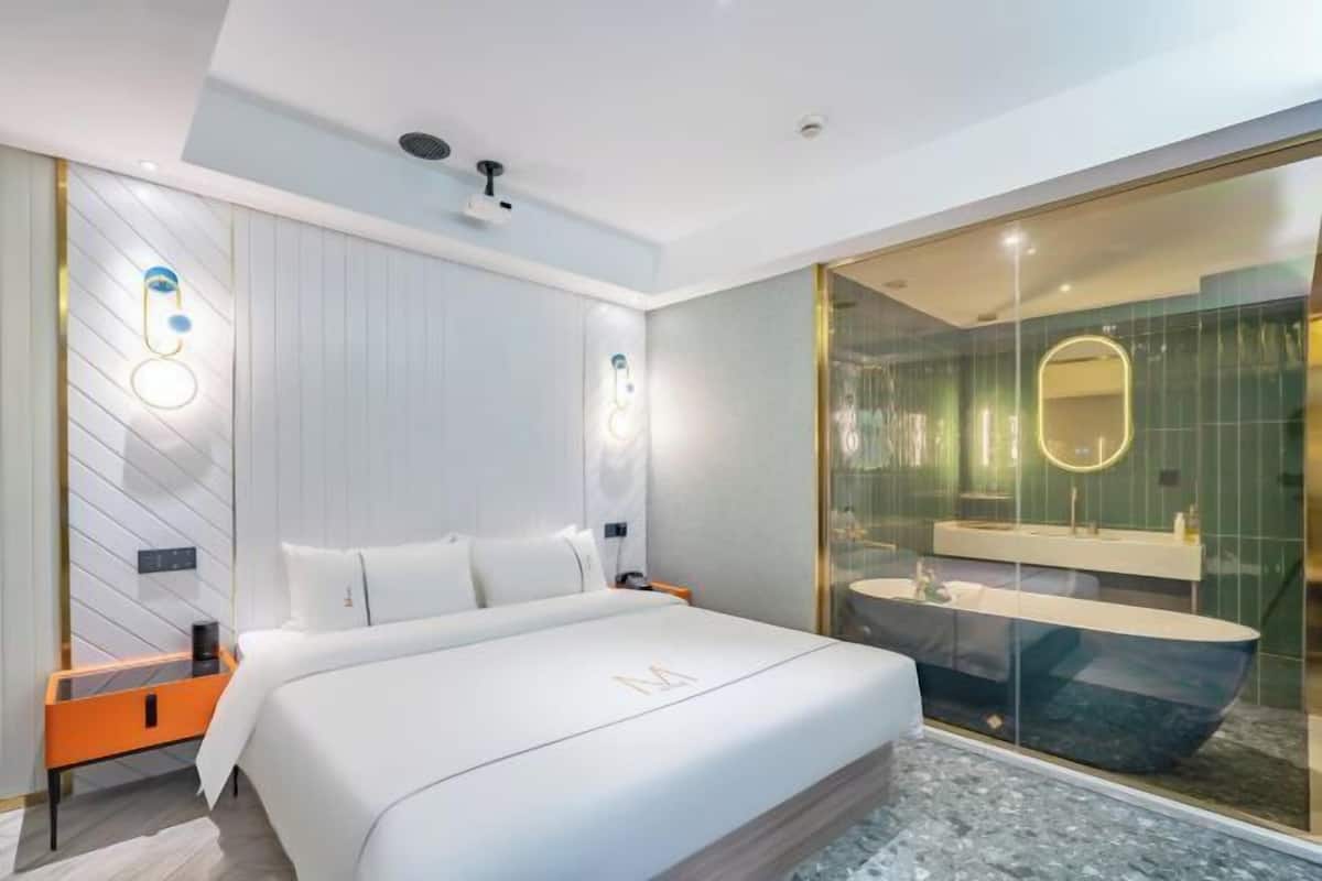 A modern hotel room with a large bed, a glass-enclosed shower, and a minimalist design.