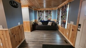 A room with a wooden ceiling, a dark sofa, and a wall with a nature-themed mural. - The Pull Down House! Brand New Utopia! (Jackman)