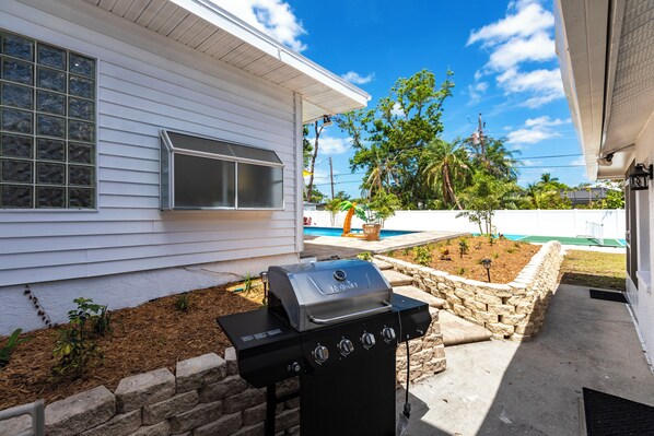 A barbecue grill in a backyard with a house, a stone wall, and a pool in the background.