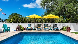 A swimming pool with blue tiles, surrounded by a white fence. There are three yellow umbrellas providing shade.