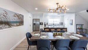 A modern kitchen with white cabinets, a stainless steel refrigerator, and a dining area with a wooden table set for six.