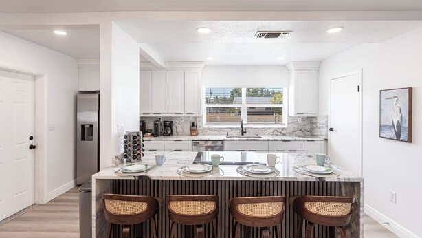 A modern kitchen with white cabinetry, a marble countertop, and a central island with bar stools.