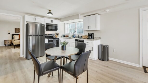A modern kitchen with white cabinets, stainless steel appliances, and a dining area with black chairs. - Pet-Friendly 1-Bed, Walk to Fluor Field & Downtown (Greenville)