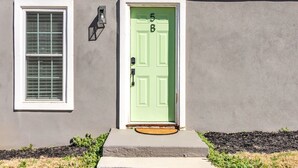 A house with a green door marked with the number 5B, a window with blinds, and a small porch area. - Pet-Friendly 1-Bed, Walk to Fluor Field & Downtown (Greenville)