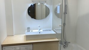 A compact bathroom with a washing machine, a sink, and a shower.