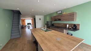A modern kitchen with a wooden island, built-in appliances, and a staircase leading to a dining area. - Complete stone house 130 m2 (Heuilley-le-Grand)