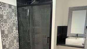 A modern bathroom with a glass-enclosed shower, a black and white patterned tile wall, a wooden floor, and a black countertop with a sink. - Complete stone house 130 m2 (Heuilley-le-Grand)