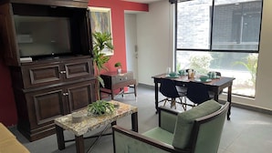 A dining area with a table set for four, a television on a cabinet, and a large window with a view of greenery. - Asombroso Departamento cerca de Santa Fe (Mexico City)