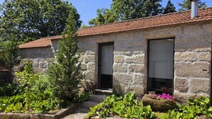 A stone building with a tiled roof, two doors, and a garden with plants and flowers.