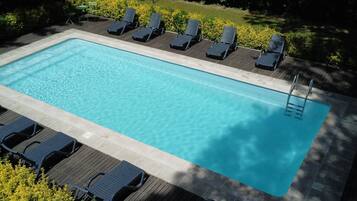 Une piscine rectangulaire à l’eau claire, entourée de chaises longues en bois et d’une terrasse en bois.
