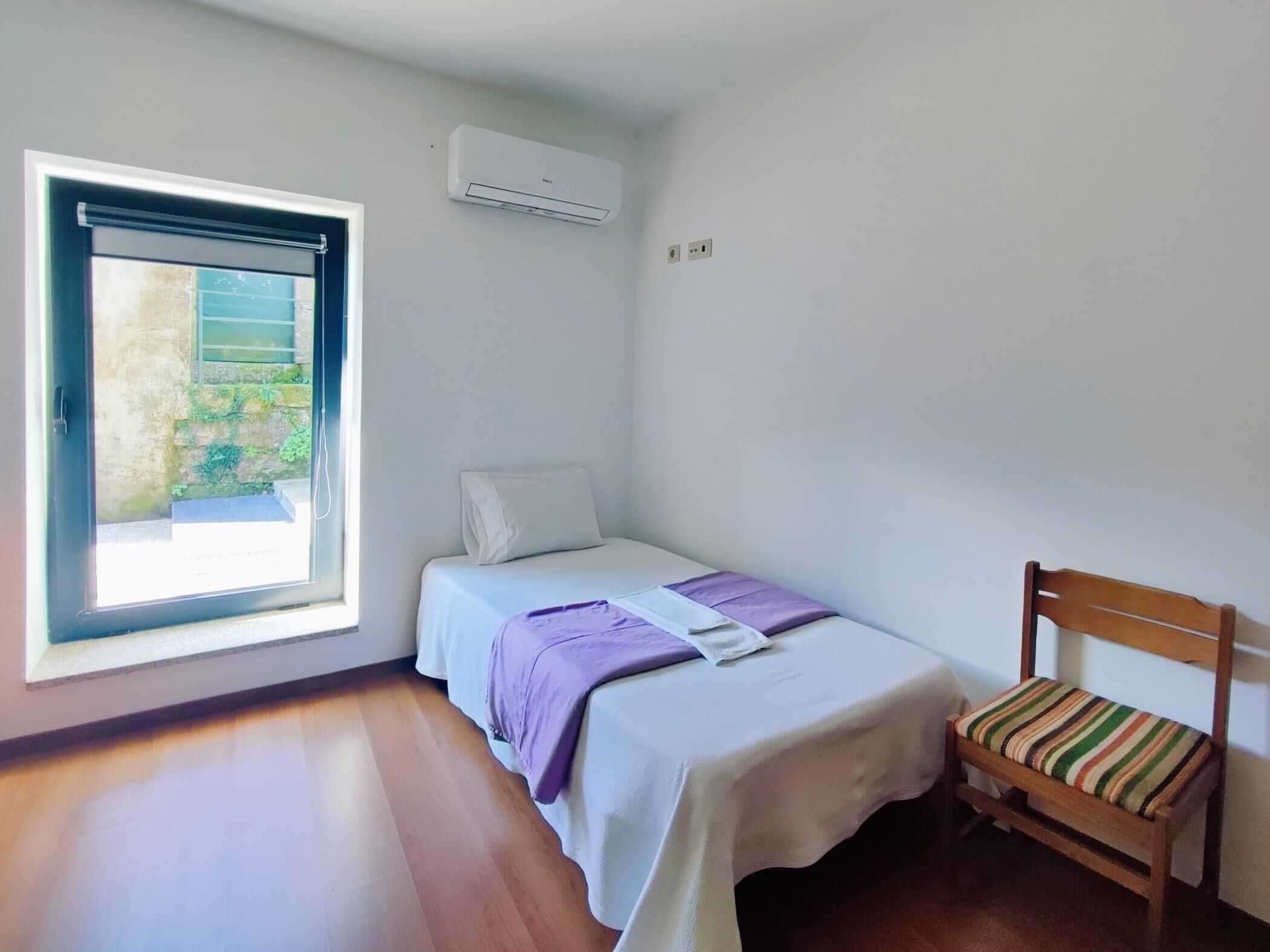 A small, clean room with a bed, a chair, and a window.