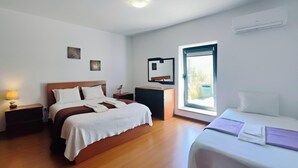 A hotel room with a double bed, a single bed, a nightstand with a lamp, a dresser, a mirror, and a window with a view.