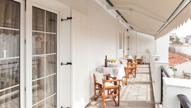A balcony with a table and chairs, a tiled floor, and a view of the city. - villa penelope (Skiathos)