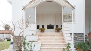 A white building with a covered entrance, a set of stairs leading to a door, and potted plants on the steps. - villa penelope (Skiathos)