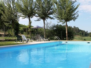 A swimming pool with lounge chairs and a table, surrounded by trees.