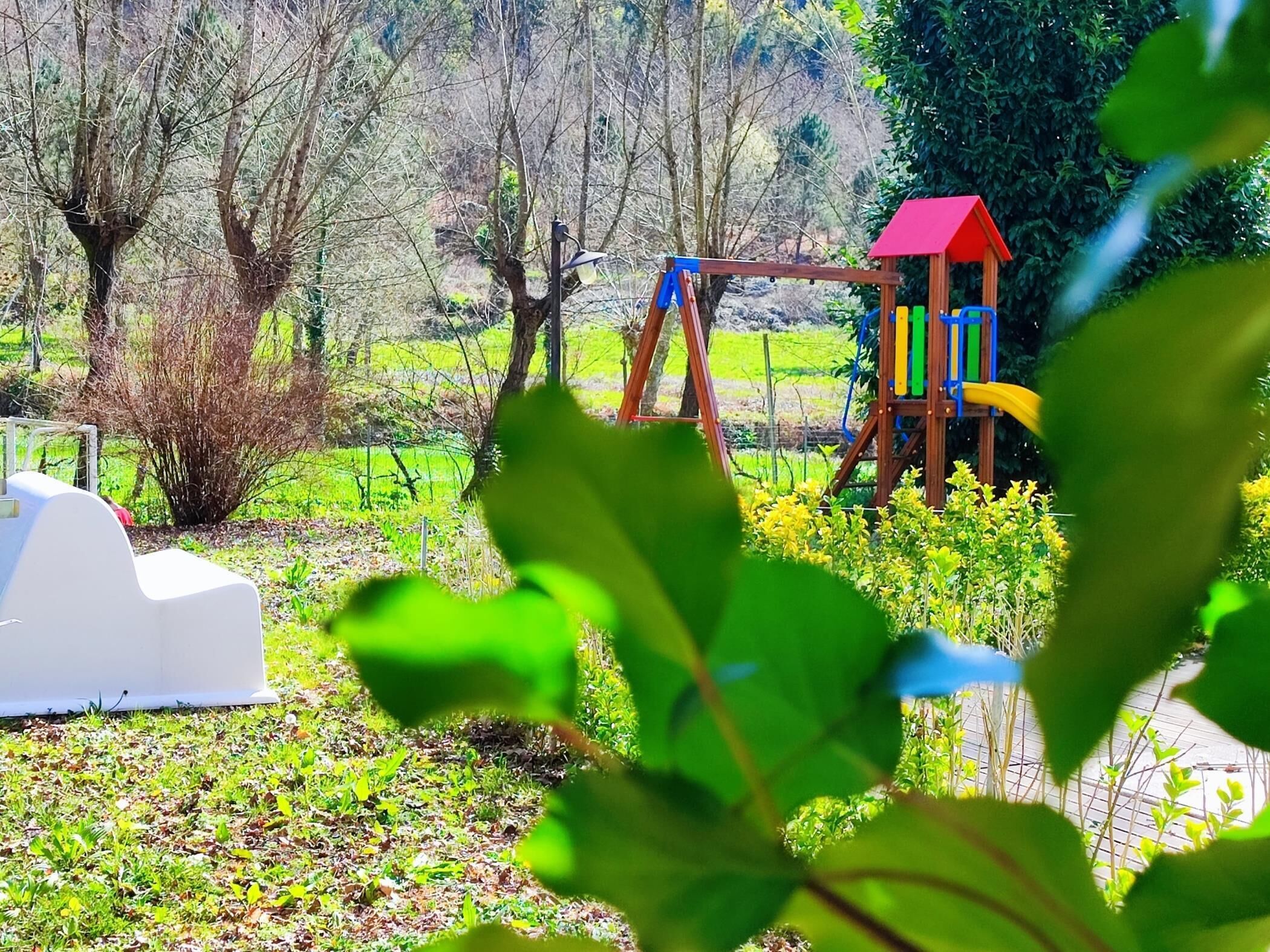 Um parquinho com balanço e escorregador, cercado por vegetação.