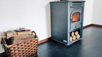 Ein Zimmer mit einem grauen Holzofen, einem gewebten Korb und einem Holzstoß.