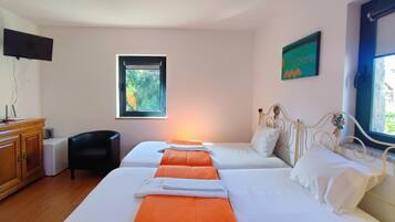Habitación de hotel con dos camas, un armario de madera, televisor, ventana con vista a follaje y un cuadro en la pared.
