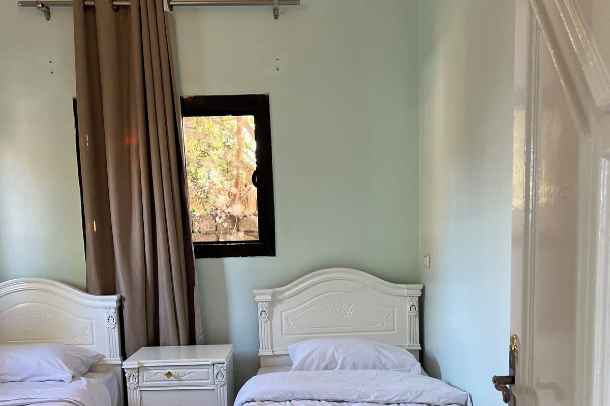A bedroom with two beds, a nightstand, a window with curtains, and a checkered floor.