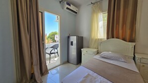 A hotel room with a bed, a small desk, a refrigerator, and a sliding glass door leading to an outdoor area. - Manzzel Dahab Hostel (Dahab)