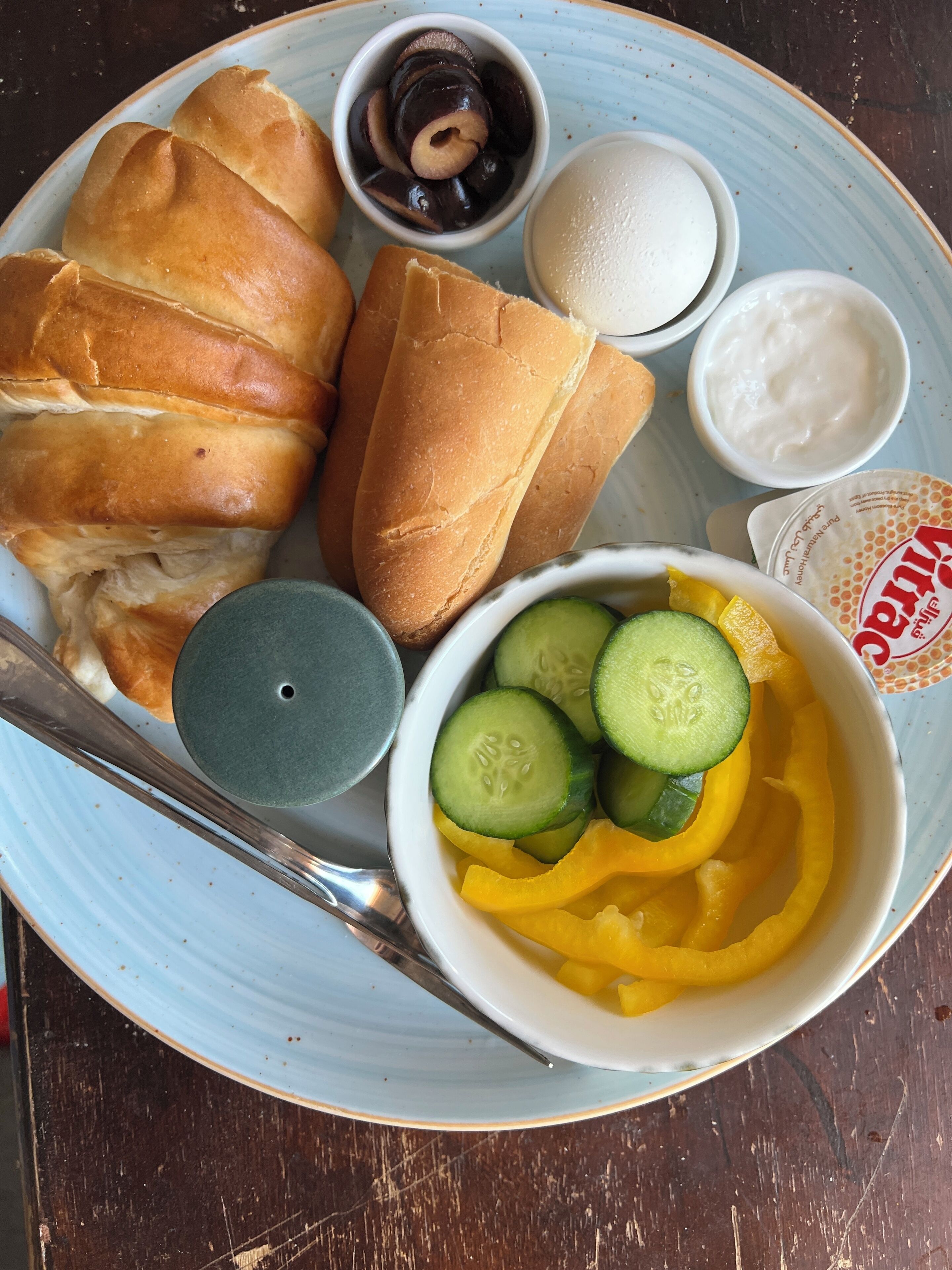 A plate with croissants, a bowl of sliced cucumbers and yellow fruit, and two small bowls of condiments.