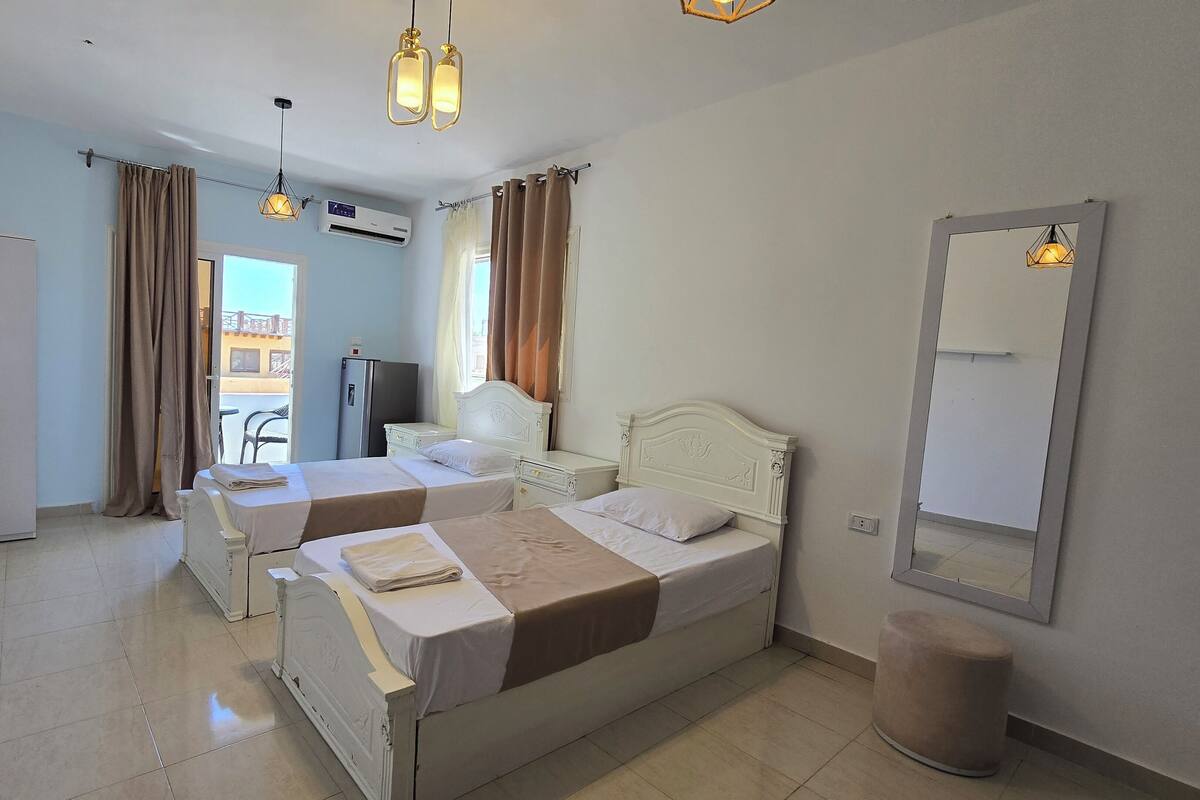A hotel room with two beds, a TV, an air conditioner, and a balcony with a view.