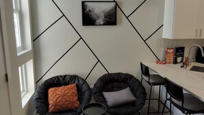 Une cuisine moderne avec un plan de travail blanc, des chaises noires et une œuvre d’art murale en noir et blanc.