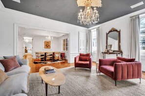A spacious living room with a chandelier, red sofas, a coffee table, and a large mirror.