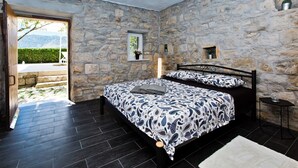 A bedroom with stone walls, a double bed, a small table, and a view of the outdoors. - Chic 3-bedroom apartment with AC, WiFi in charming Žrnovnica (Žrnovnica)