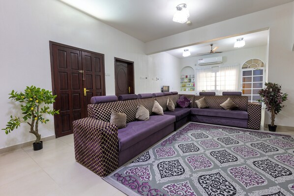 Un salón con un sofá morado, una alfombra estampada y una planta en maceta.