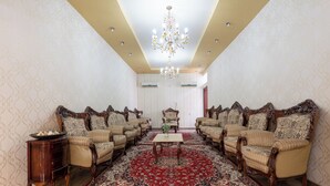 A formal room with a large red carpet, multiple upholstered chairs, a central table, and a chandelier. - Bait Allubana Villa (Seeb)
