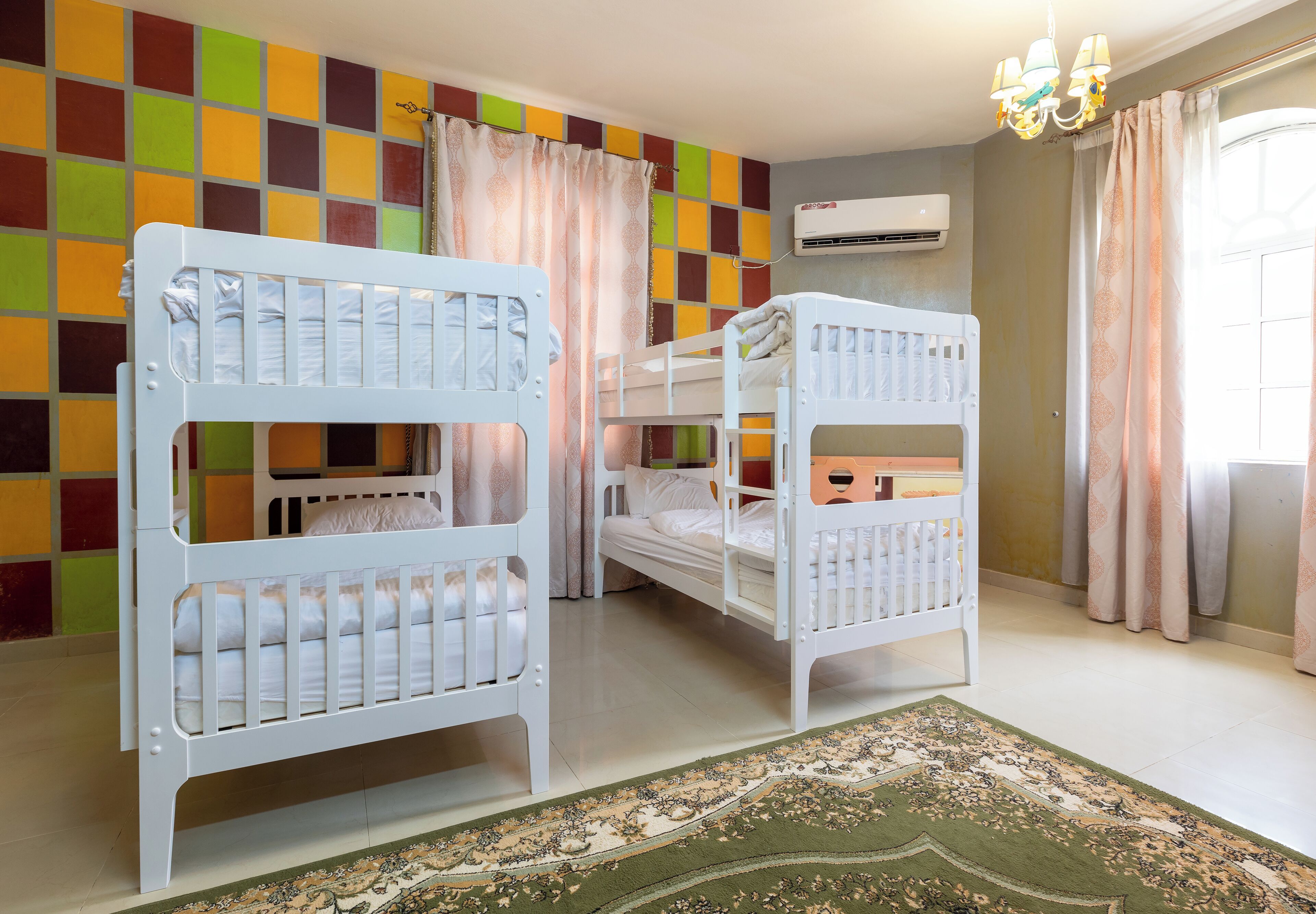 A room with two bunk beds, a patterned rug, and a colorful wall.