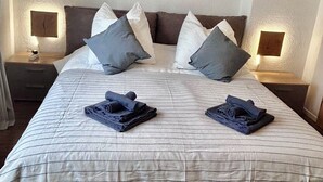 A neatly made bed with a striped bedspread, two pillows, and folded towels on the bed. There are two bedside tables with lamps on either side of the bed. - Apartment near Hannibal Center (Bochum)