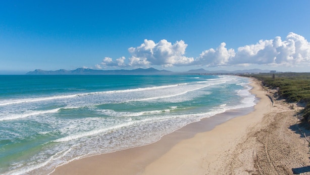 Une plage avec un rivage sablonneux, des vagues et des montagnes lointaines sous un ciel dégagé.