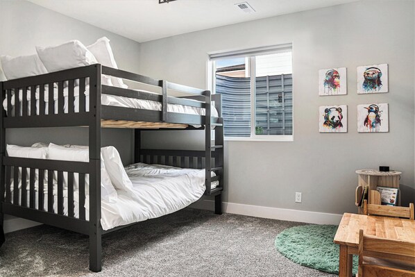 A bunk bed room with a window, artwork on the wall, and a small table with a chair.