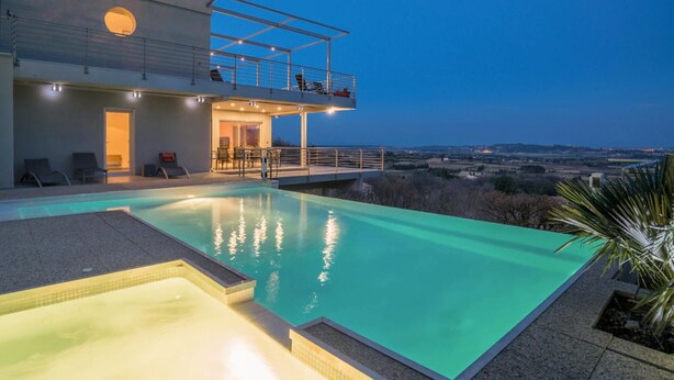 Ein moderner Außenpool mit freiem Blick auf die umliegende Landschaft, einem überdachten Sitzbereich und einem Balkon mit Geländer.
