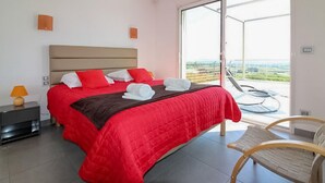 Ein Hotelzimmer mit einem großen Bett, einem Sessel, einem Nachttisch und Blick ins Freie.