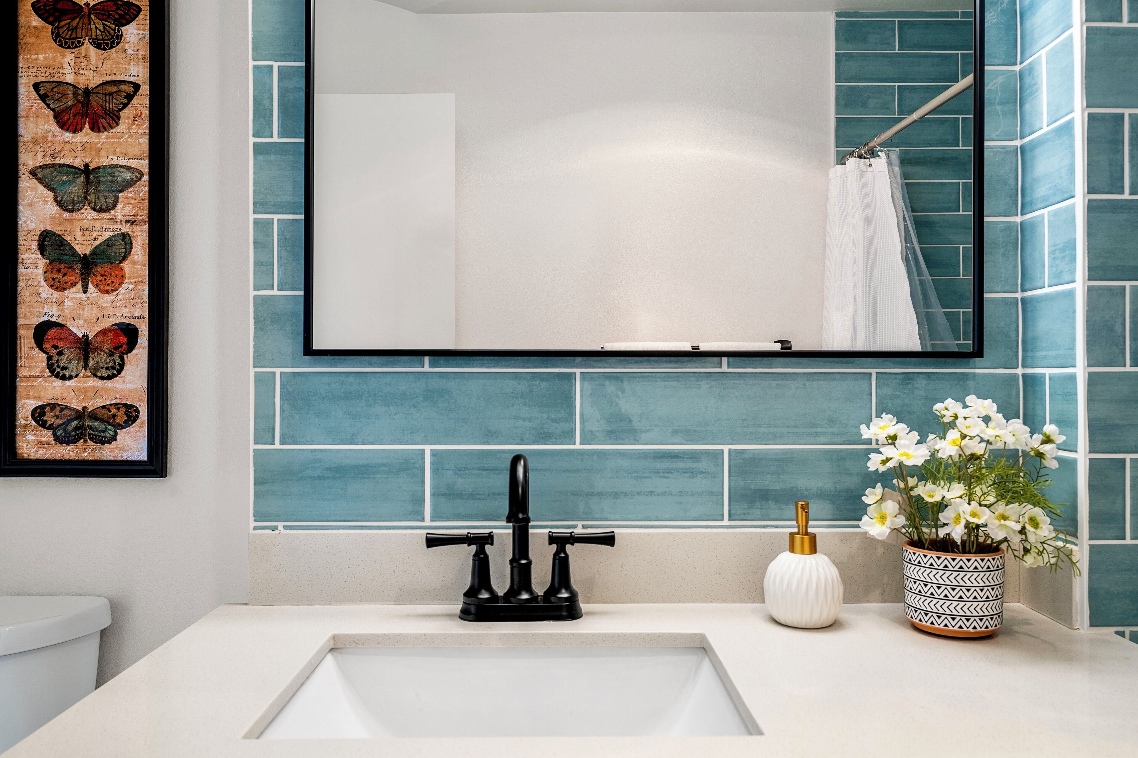 Une salle de bain avec un lavabo blanc, un robinet noir, un miroir et un mur recouvert de carreaux bleus.