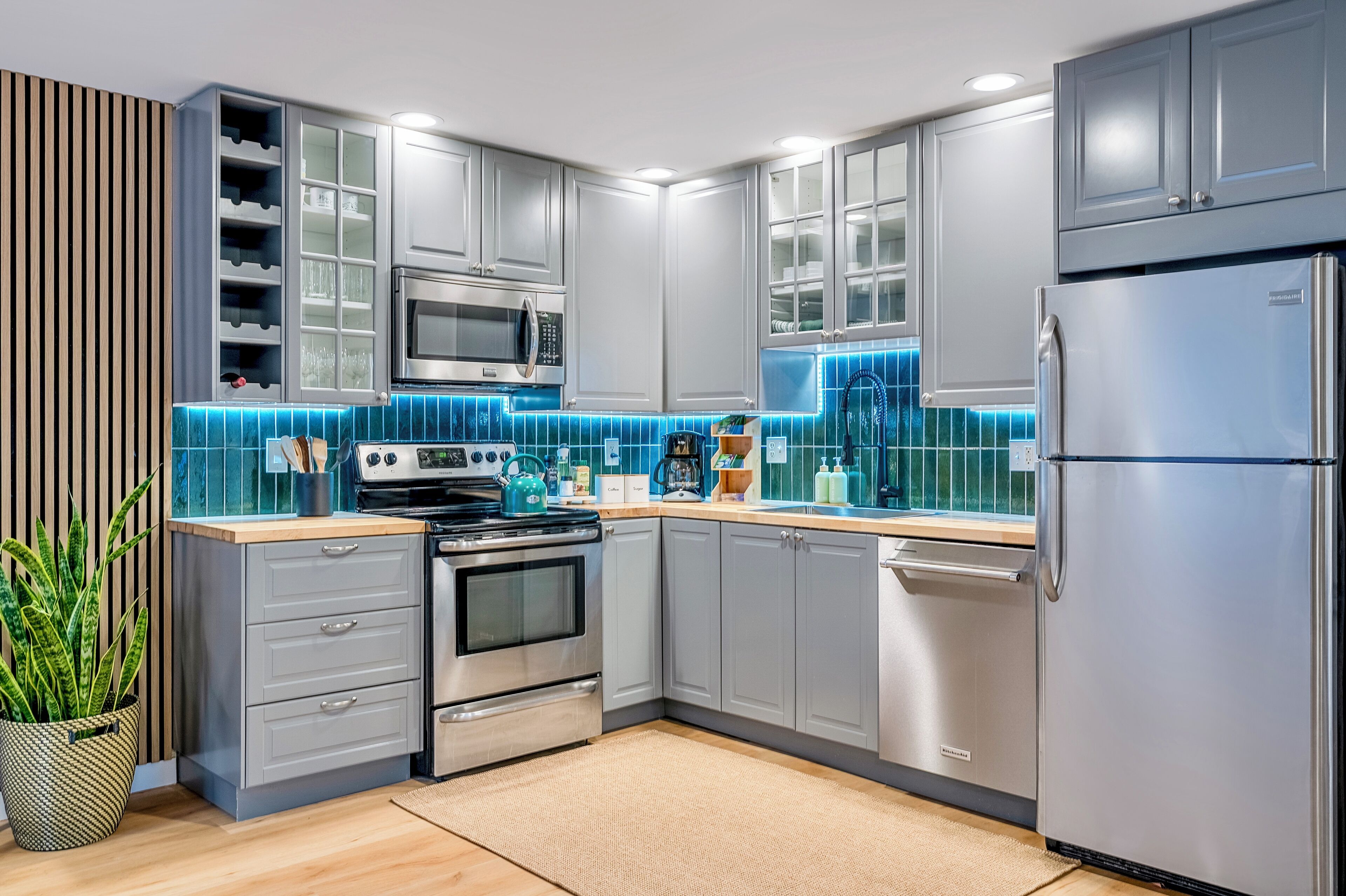 A modern kitchen with grey cabinets, stainless steel appliances, and blue-tiled backsplash.