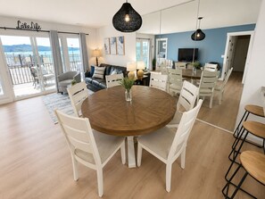 Ein modernes Wohnzimmer mit einem runden Holzes Esstisch, weißen Stühlen, einem Sofa und einem Balkon mit Blick.