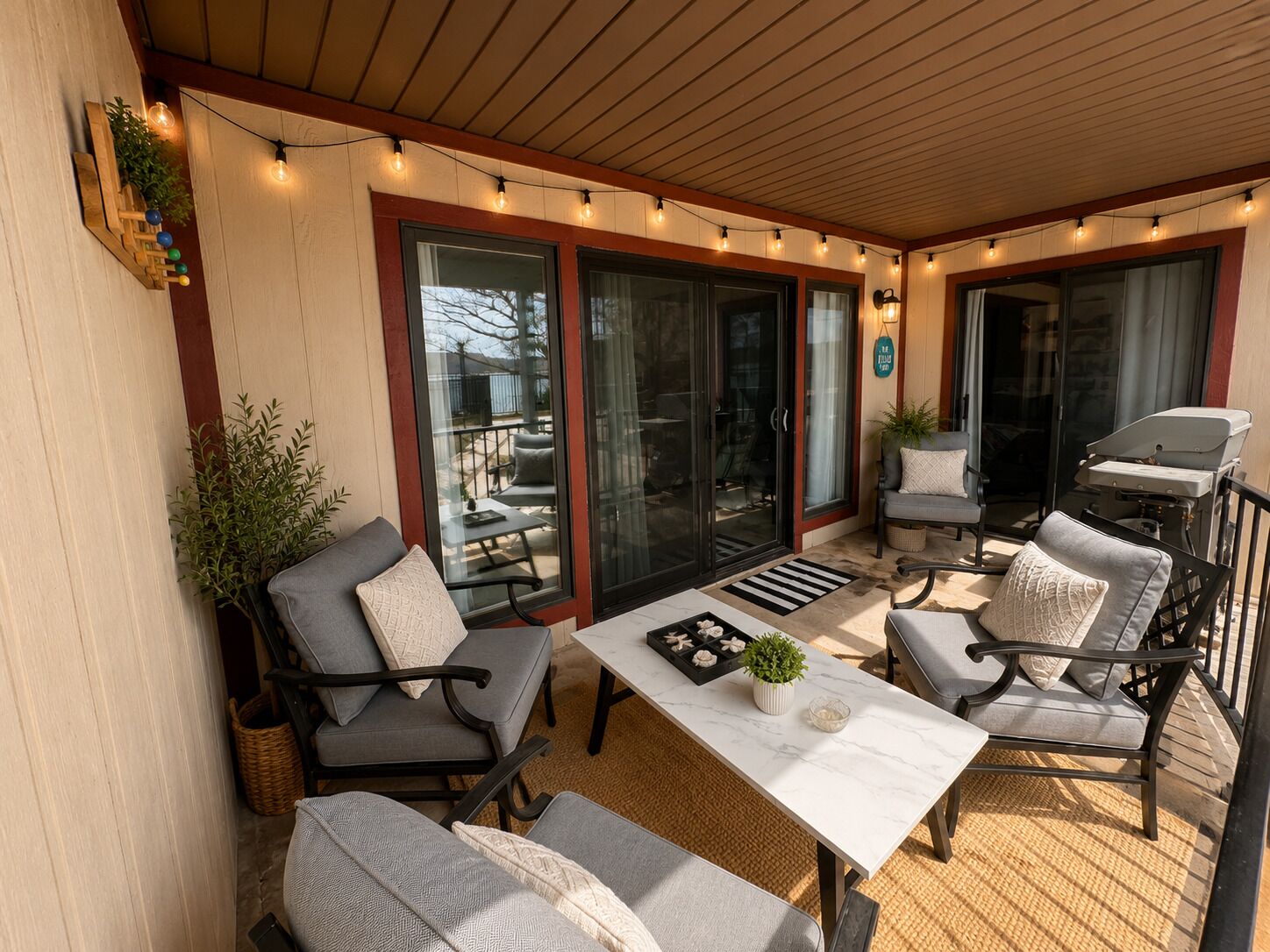 An outdoor patio with a table, chairs, string lights, and a grill.